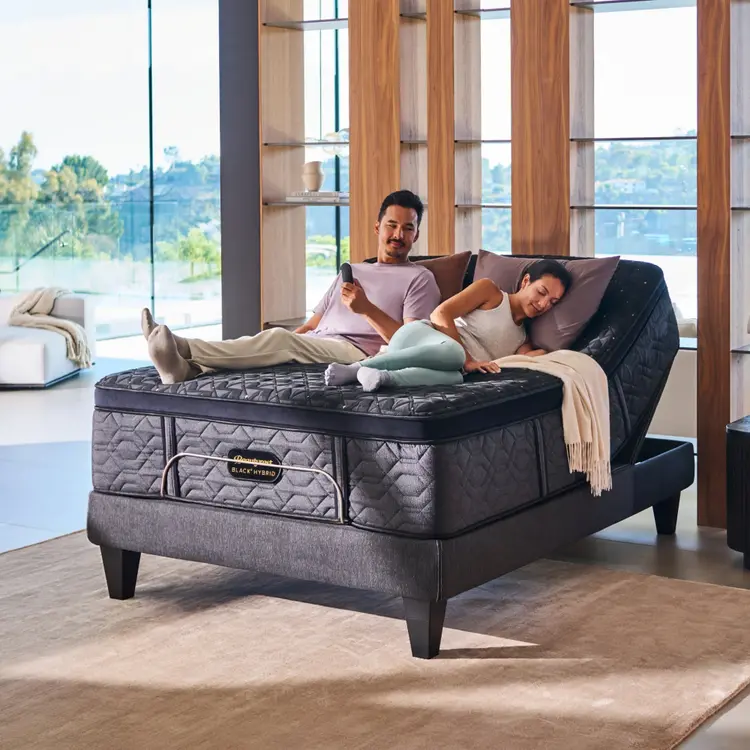 A man and woman laying on a BeautyRest Plush Apex Top Hybrid mattress sitting on an adjustable base || series: Series Four || feel: Plush Apex Top
